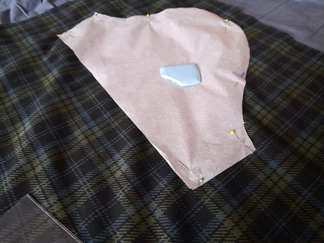 A pattern piece pinned onto fabric for cutting, with a dressmaking chalk tool placed on top.
