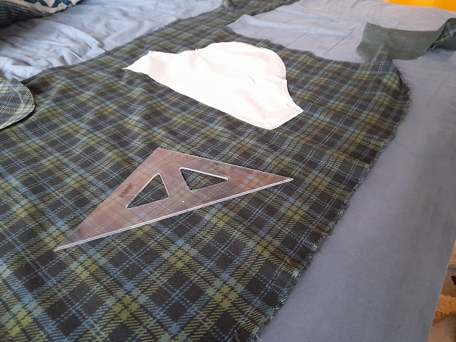 A sewing project featuring a piece of plaid fabric with a white pattern piece and a ruler on a table.