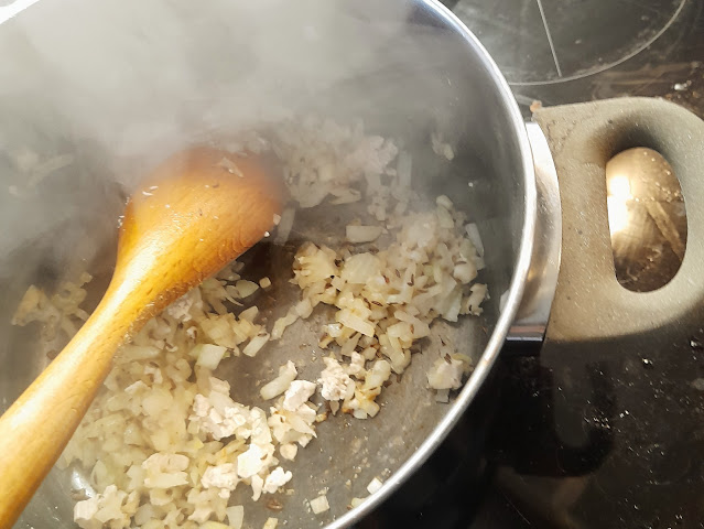 Chopped onions sautéing in a pot with steam rising, with a wooden spoon resting against the pot.