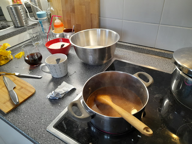 A kitchen counter with various utensils, bowls, and a pot of steaming soup cooking on the stove, illustrating the preparation of Slovak yeast soup.