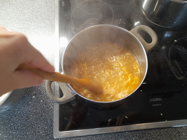 A hand stirring boiling yeast soup in a pot on a stovetop, with steam rising.