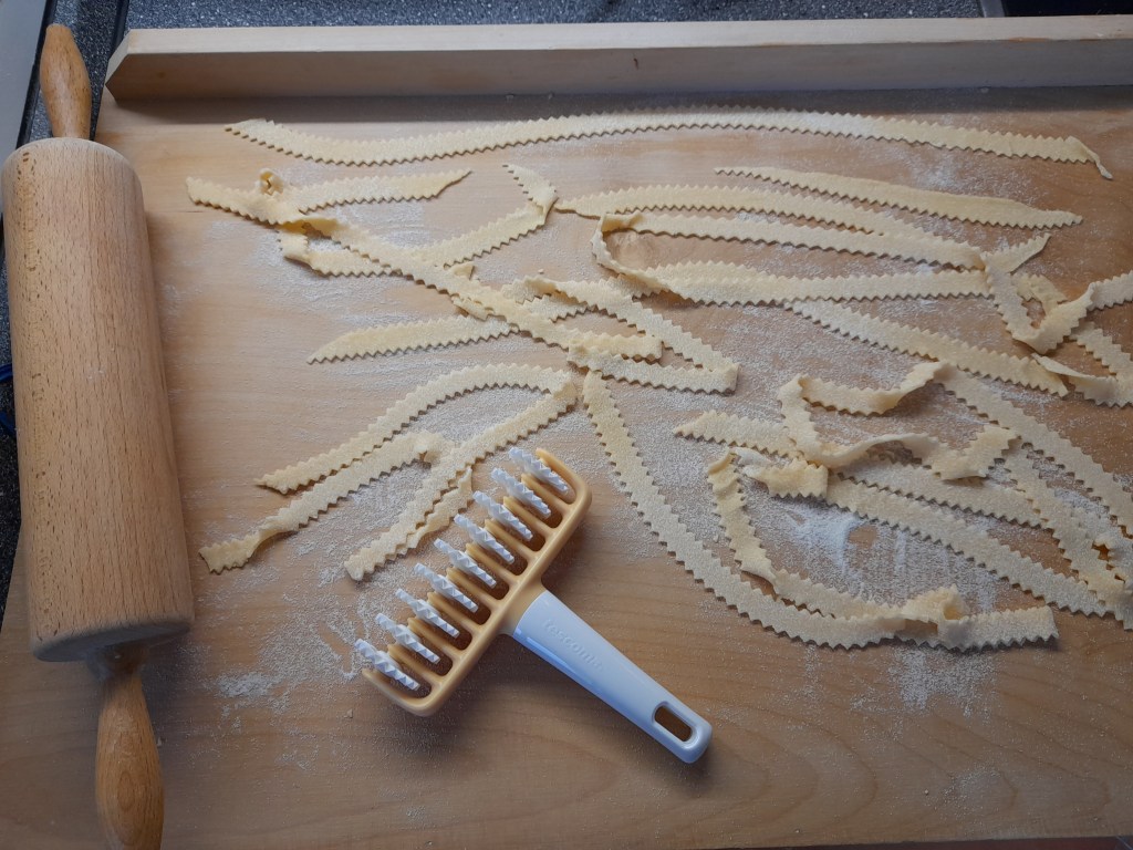 A wooden rolling pin and a multi-purpose cutter rests on a floured surface with freshly cut pasta strips laid out.