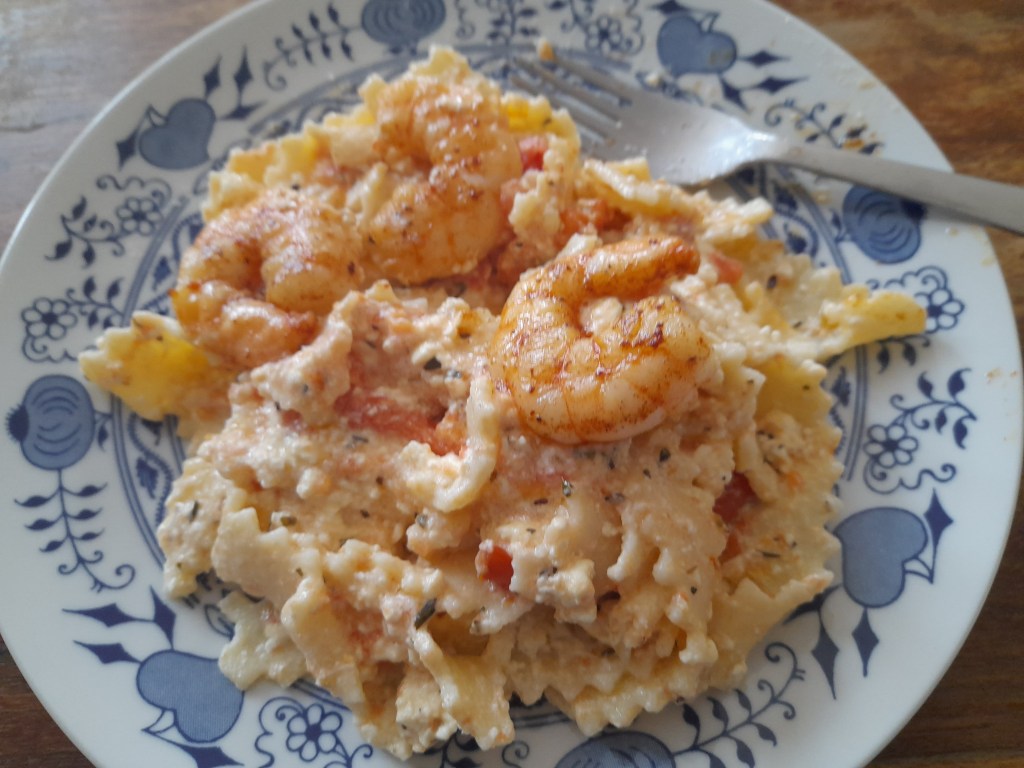 A plate of homemade pasta topped with a creamy cheese and tomato sauce, featuring shrimp, served with a fork on the side.