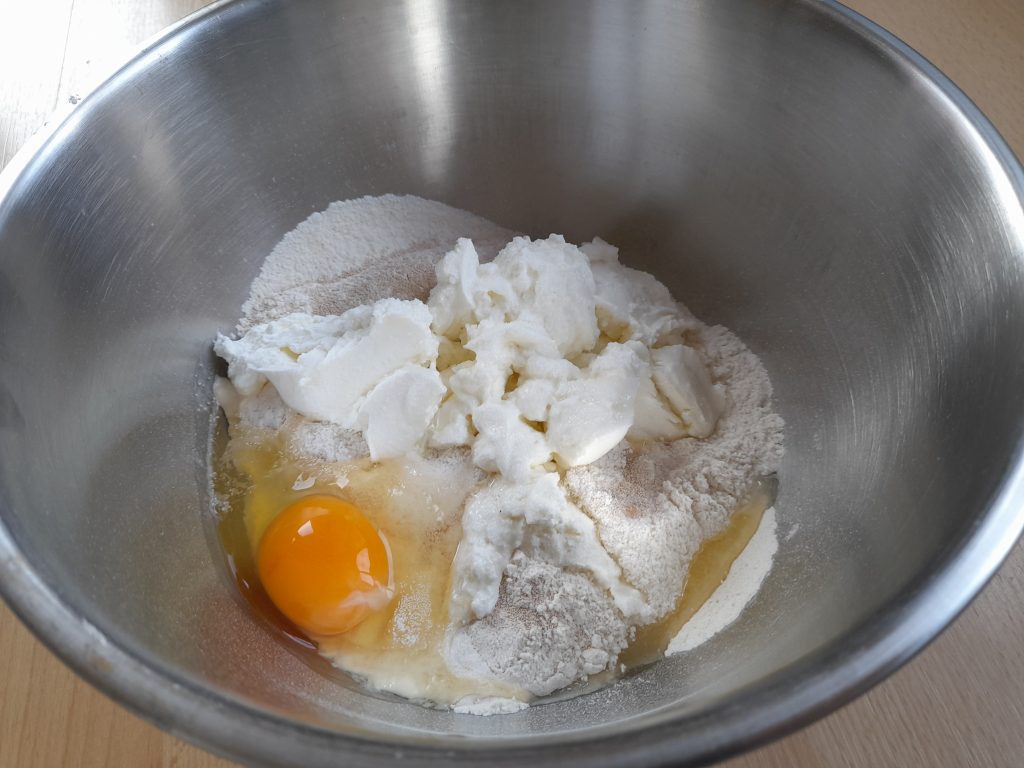 A mixing bowl containing semi-coarse flour, quark, an egg, and yeast for preparing škvarkové pagáče dough.