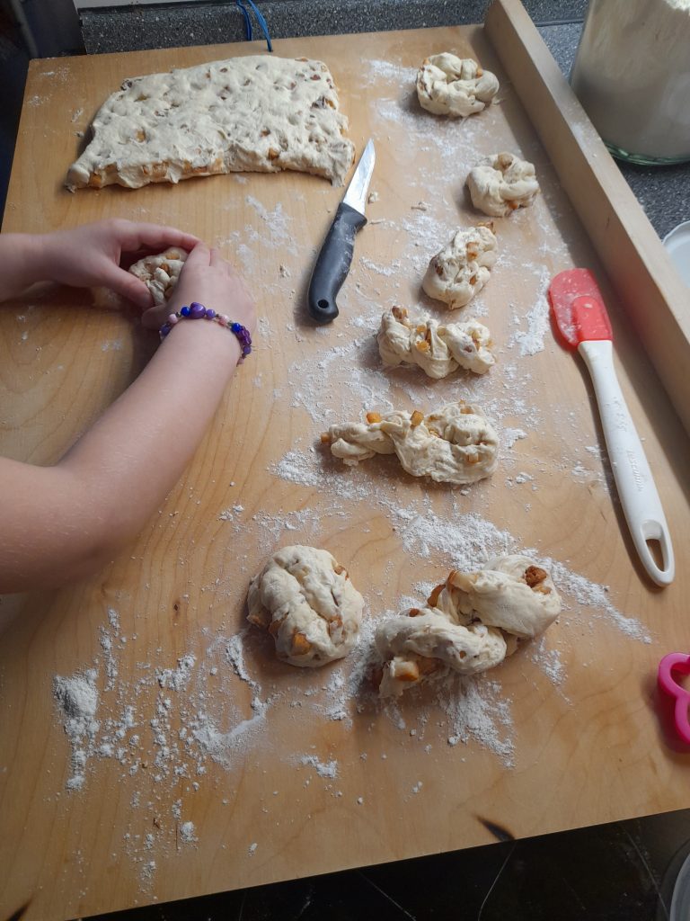 A person shaping dough on a floured wooden surface, with pieces of dough being formed into savory Slovak pastries.