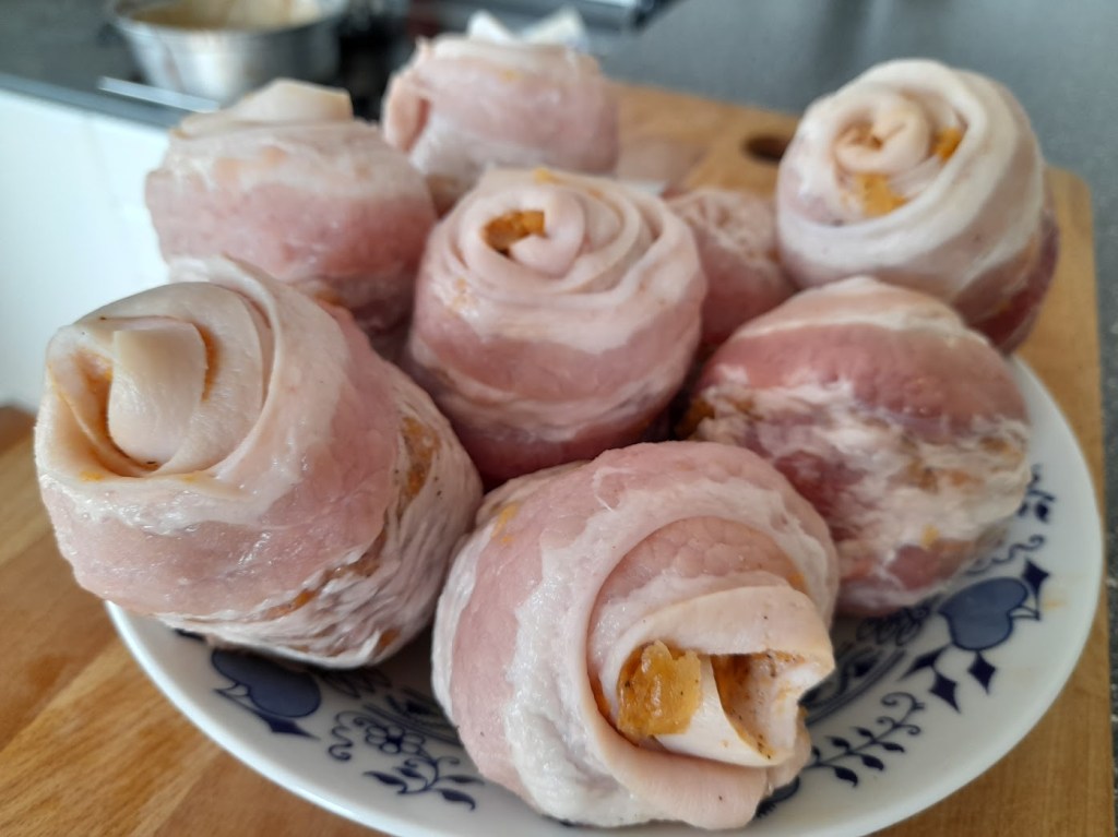 A plate of rolled pork belly stuffed with a savory mixture, showcasing spirals of bacon and meat, ready for cooking.