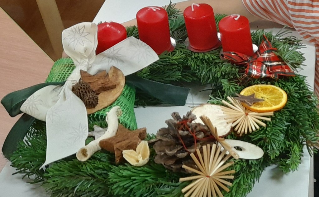 A decorated Advent wreath featuring red candles, natural elements like dried orange slices, pine cones, and wooden decorations, representing a Christmas tradition.