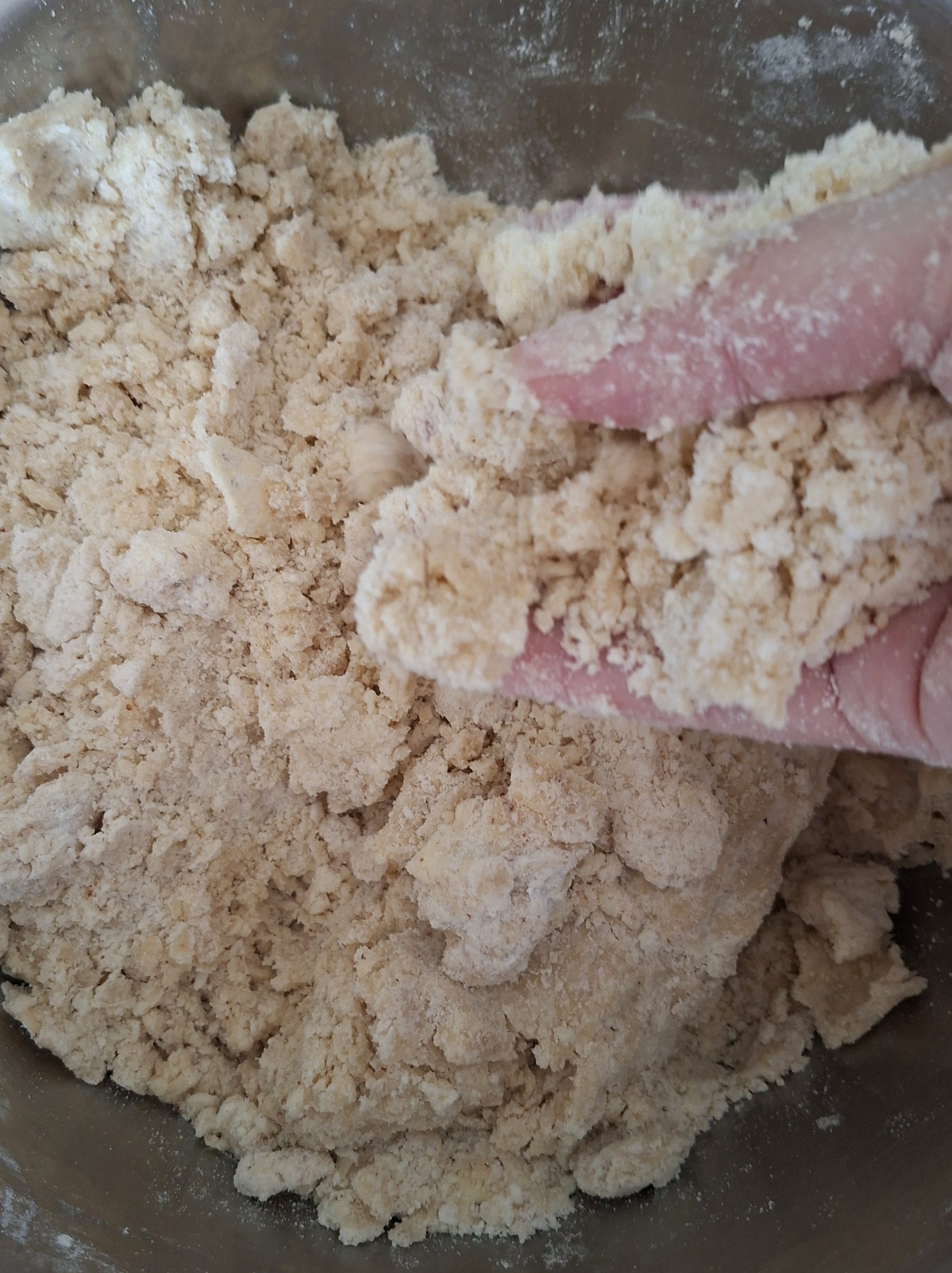 Close-up of a hand mixing crumbly dough in a metal bowl, illustrating the process of preparing traditional cookie dough for Christmas baking.