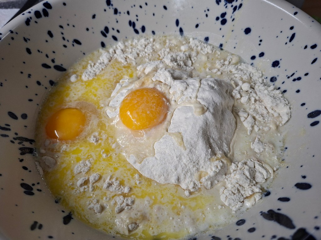 A bowl with two eggs, flour and melted butter.